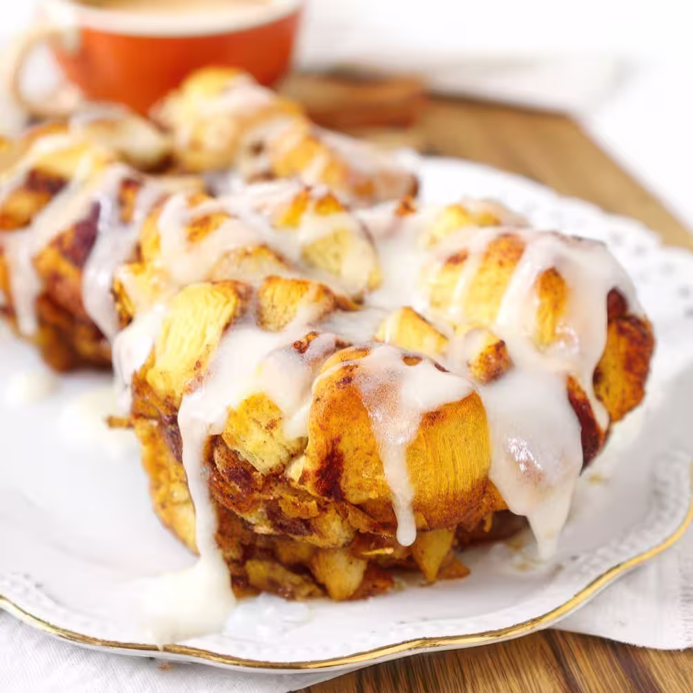 Apple monkey bread served on a white plate with icing drizzled on top.
