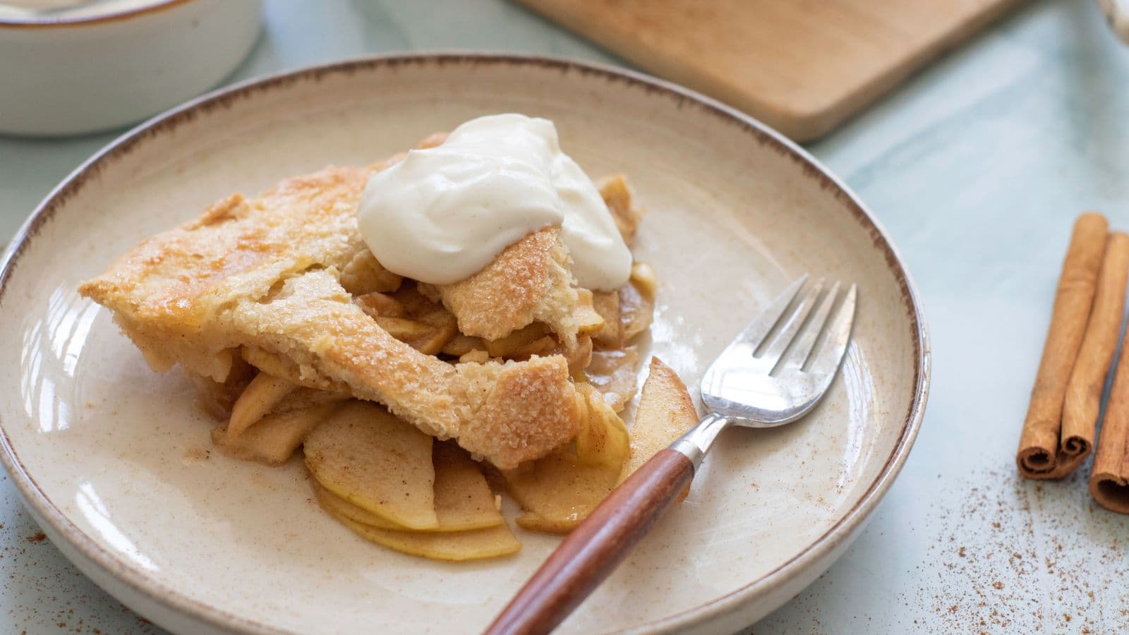 A slice of homemade apple pie served on a rustic plate with a dollop of whipped cream.