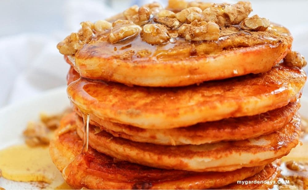 Stack of golden pumpkin pancakes topped with maple syrup, and walnuts.