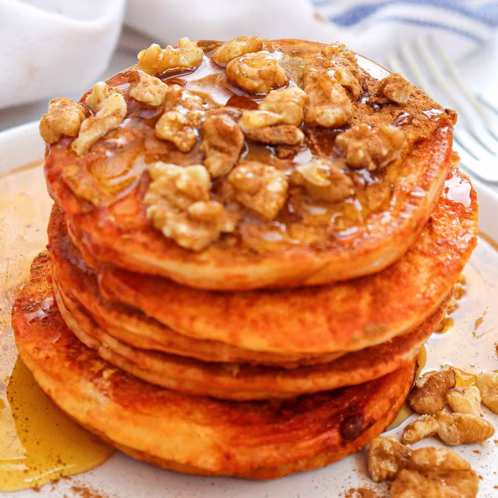 a stack of pumpkin pancakes with maple syrup and walnuts