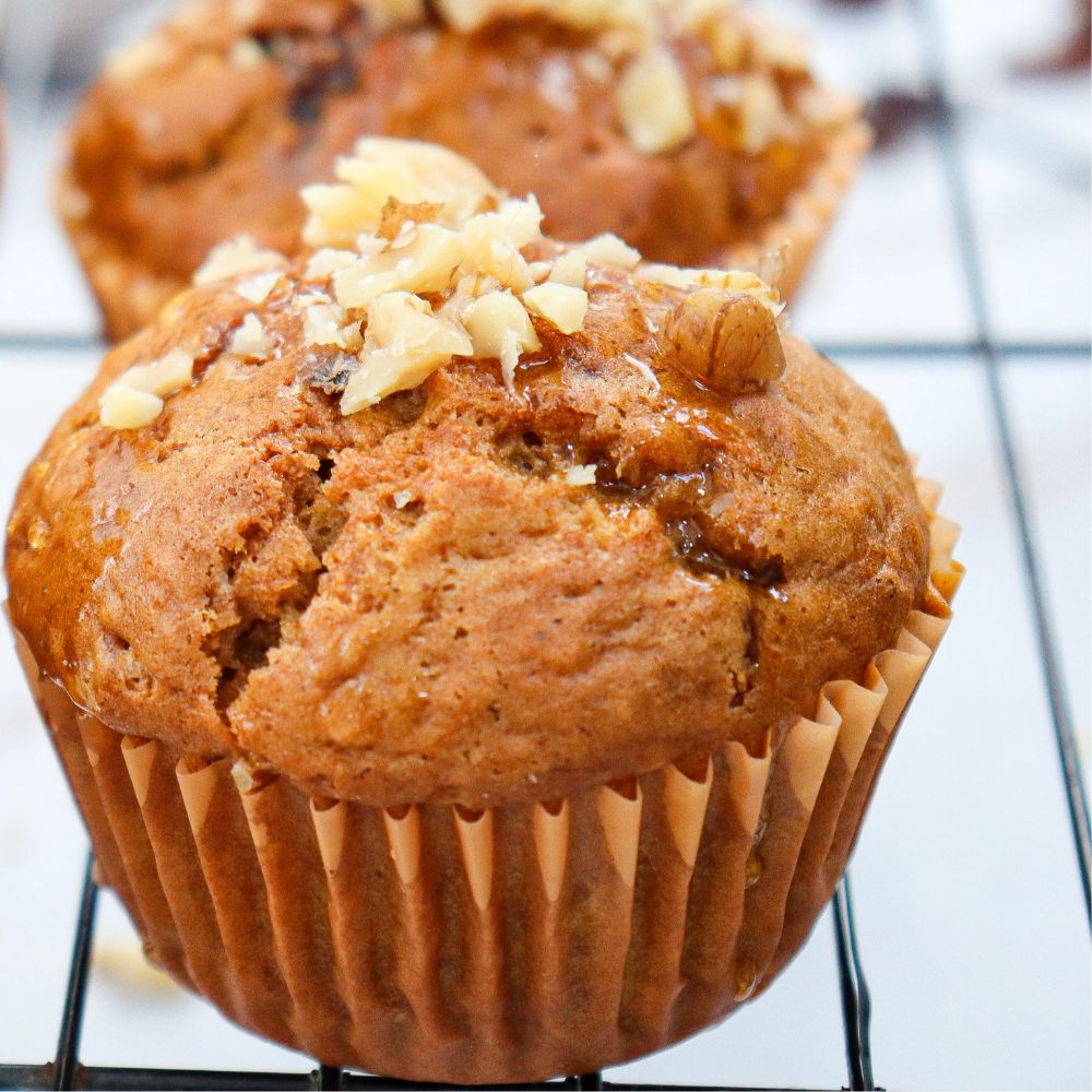Close-up of golden brown carrot muffins topped with chopped walnuts cooling on a wire rack