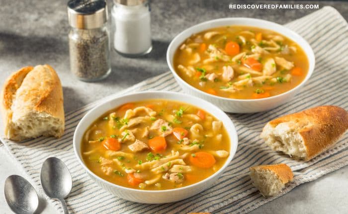two bowls of heart chicken noodle soup served with bread