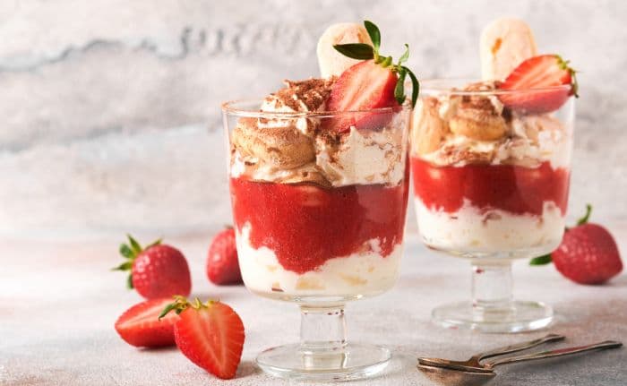 two individual servings of strawberry tiramisu garnished with strawberry and cocoa