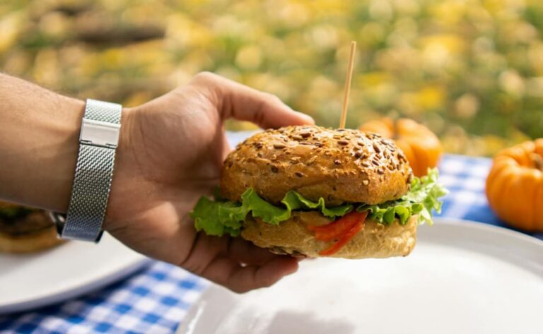 A close up of hand holding a hamburger over a picnic table