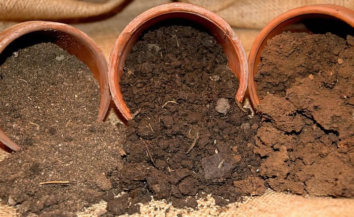 Three terracotta pots with different types of soil tipping out of each one